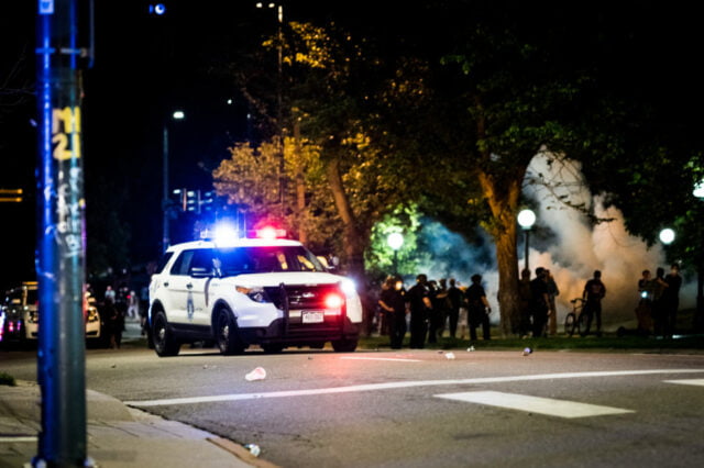 Parked police vehicle with uniformed officers gathering beside it.