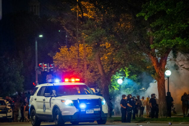 Parked police vehicle with uniformed officers gathering beside it.