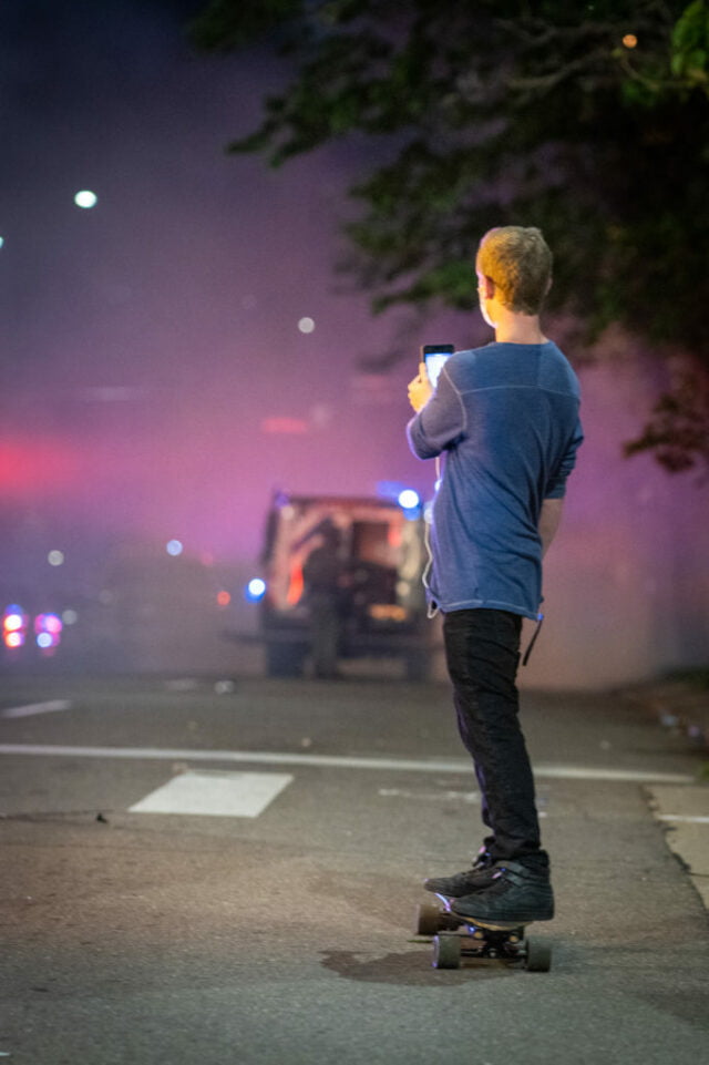 Man on skateboard with back to camera filming protest.