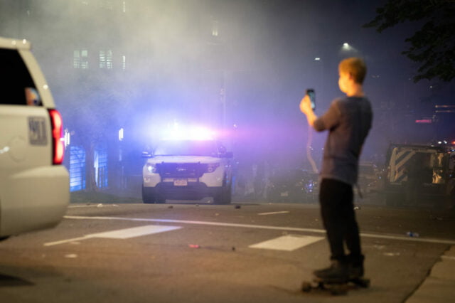 Man on skateboard with back to camera filming protest.