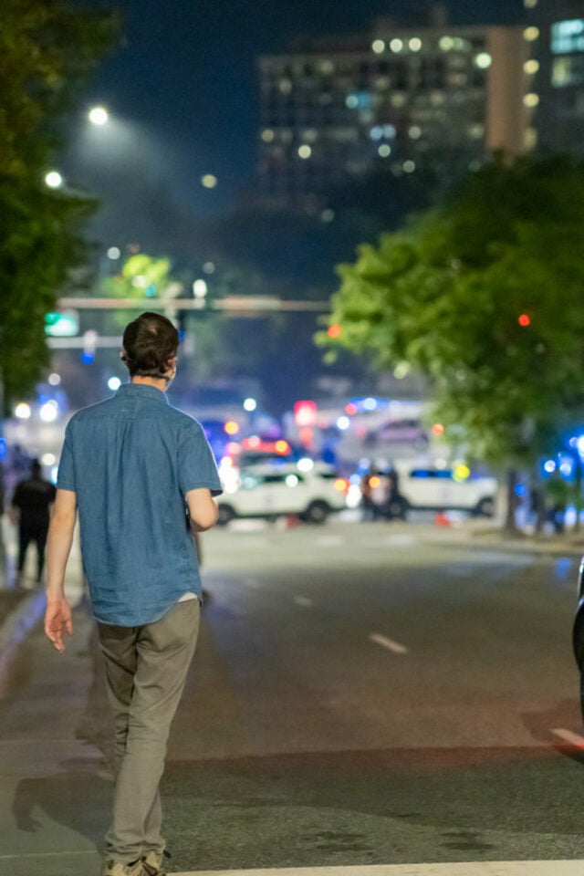 Male pedestrian watches protest site from afar.