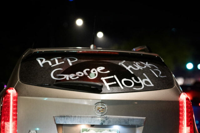 Night time back window of tan SUV with "RIP George Floyd" and "Fuck 12" written in white letters on back window