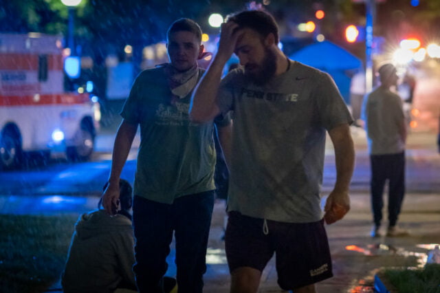 Two male protestors looking tired with protest, ambulance and police lights in the background