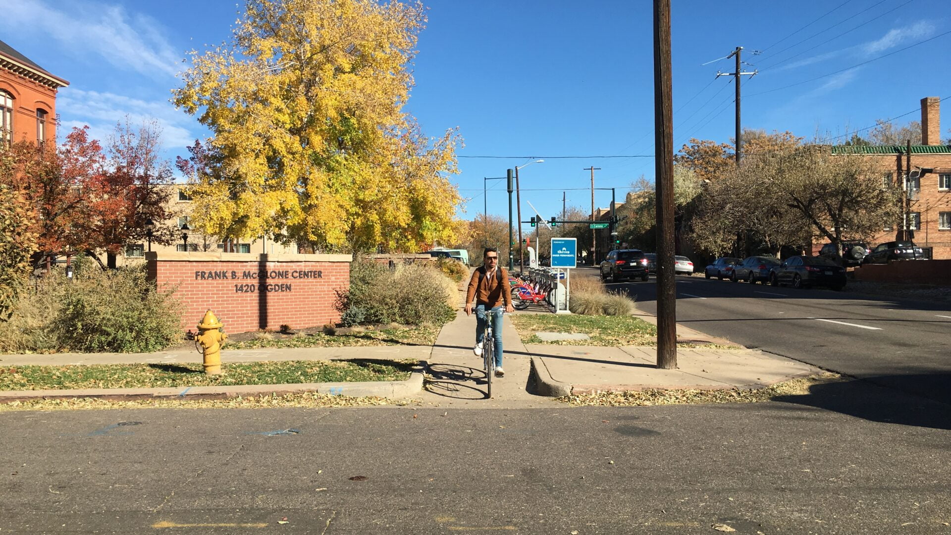 daytime. biker on sidewalk is crossing the street in front of the "Frank C. McGlone Center" sign at 140 Ogden street front of the