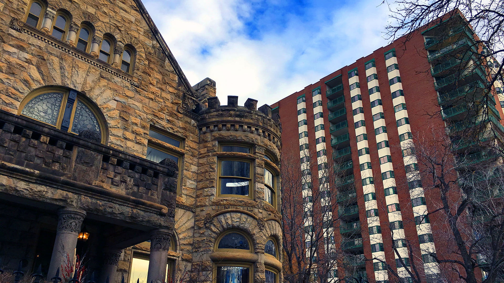 Historic brick building next to high-rise residential building. Sky is blue and partly cloudy. Trees in foreground are bare indicating winter