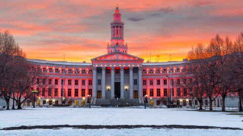 City and County of Denver building lit up red with sunset in background